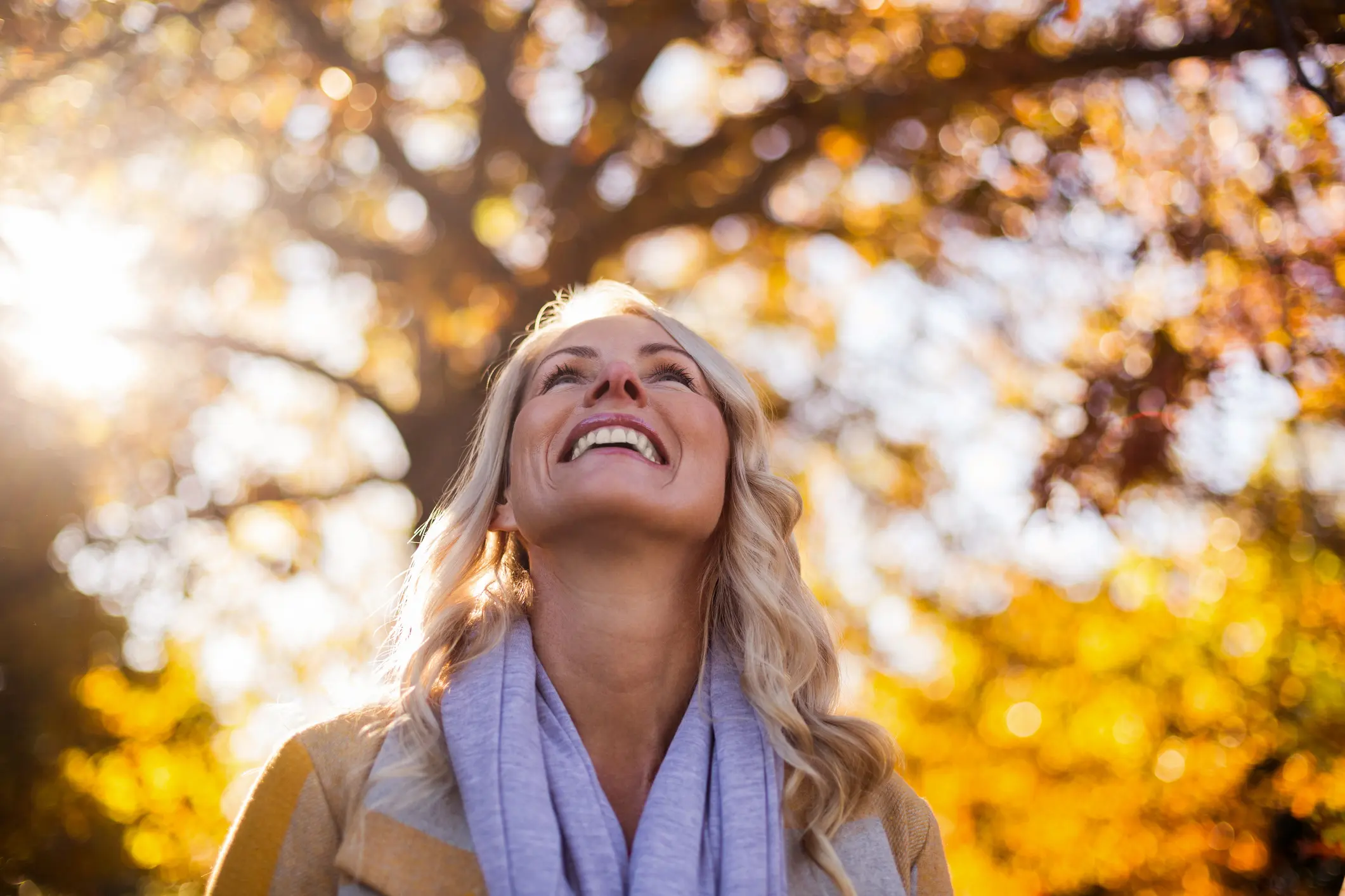 Woman smiling outdoors with autumn leaves in the background.