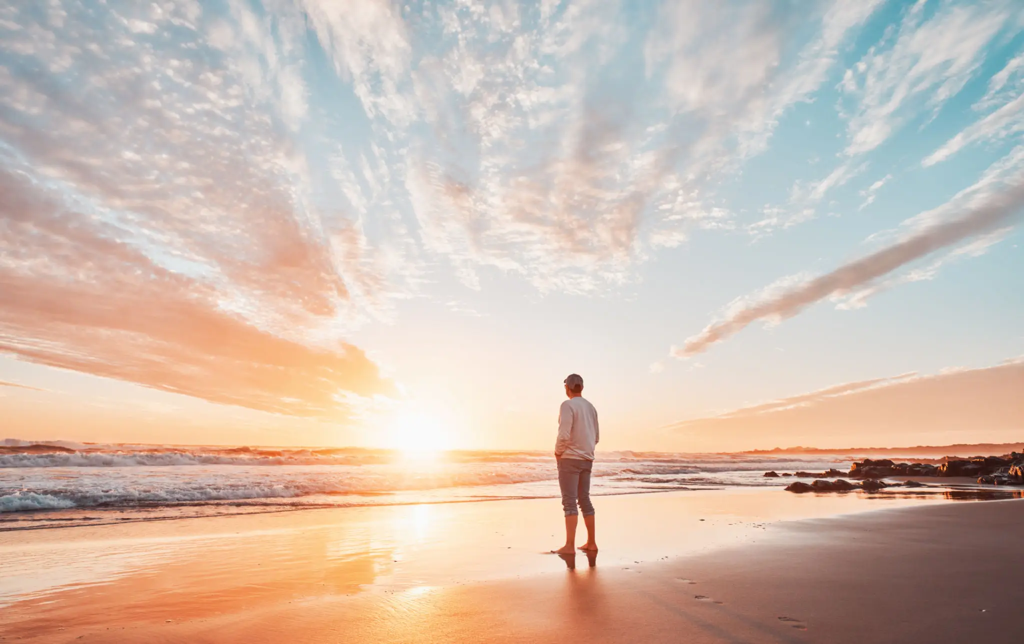 Person standing on a beach during sunset with calm waters.