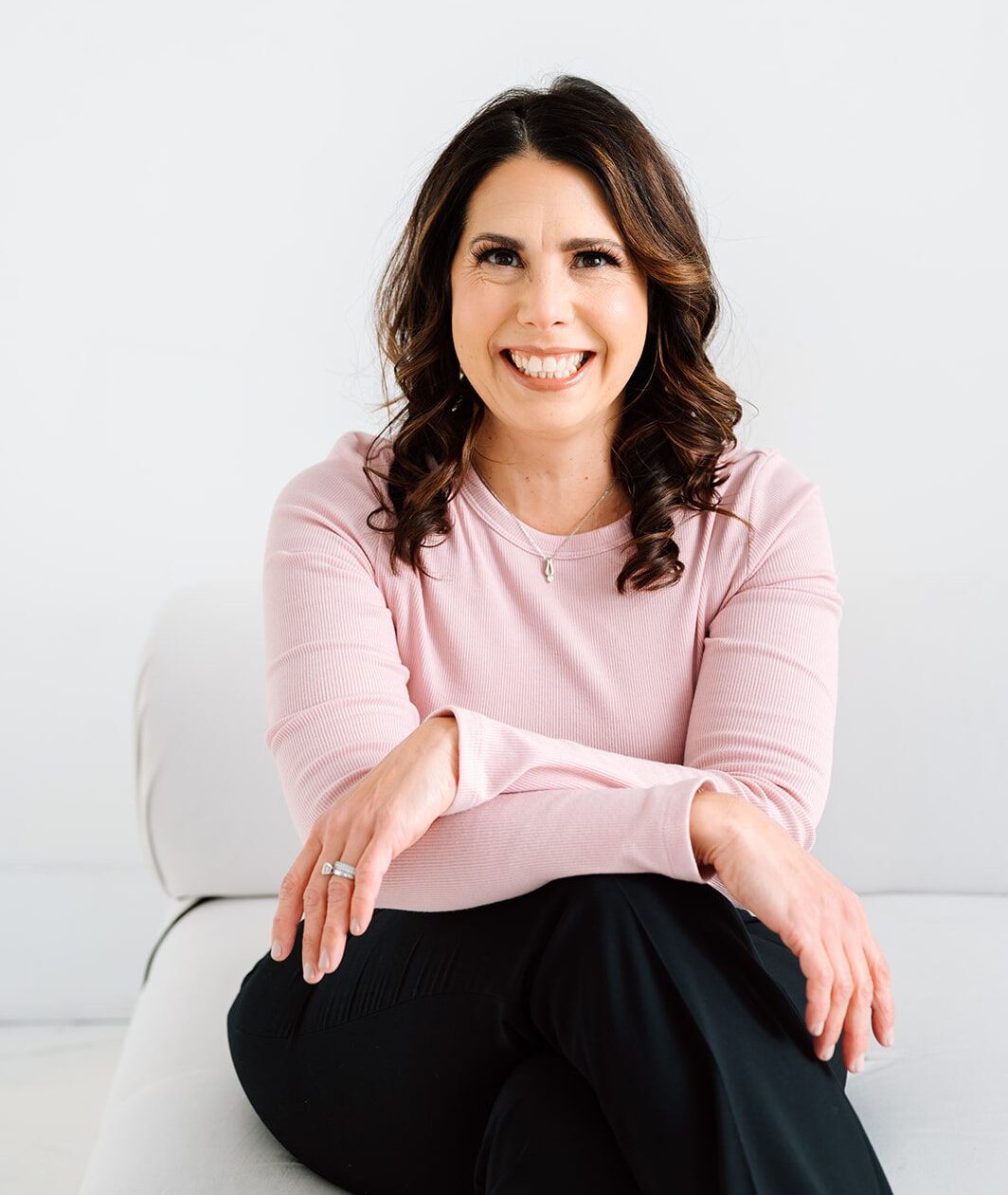 Smiling woman in pink sweater sitting comfortably against a white background.